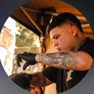 Nahuel cortando el pelo con guantes negros, con tatuajes en el brazo